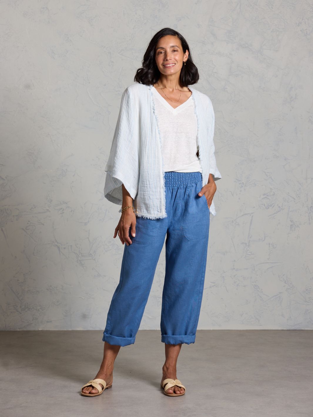 Woman wearing a white top and blue pants against a gray background